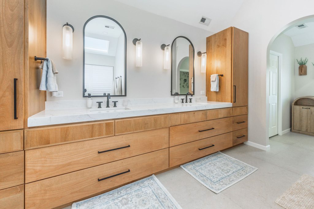 Wood vanity with double sinks, arched mirrors, and matte black fixtures in a spa-like primary bathroom remodel