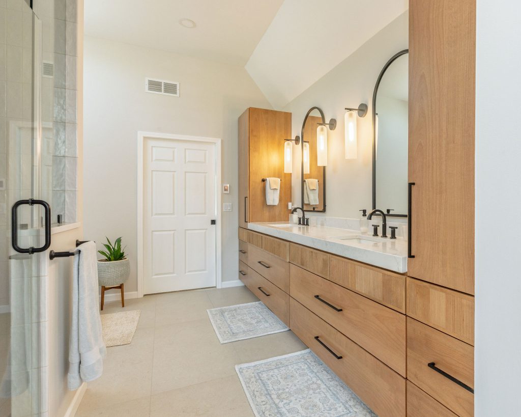 Double vanity with arched mirrors opening toward the hallway that connects to the primary closet