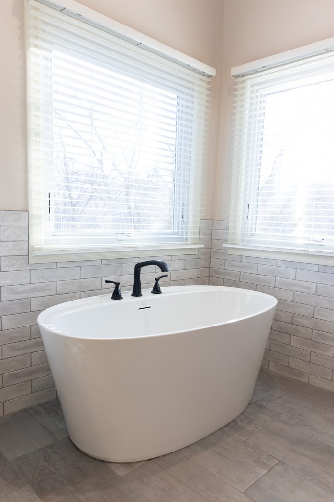 Freestanding soaking tub positioned near corner windows with natural light