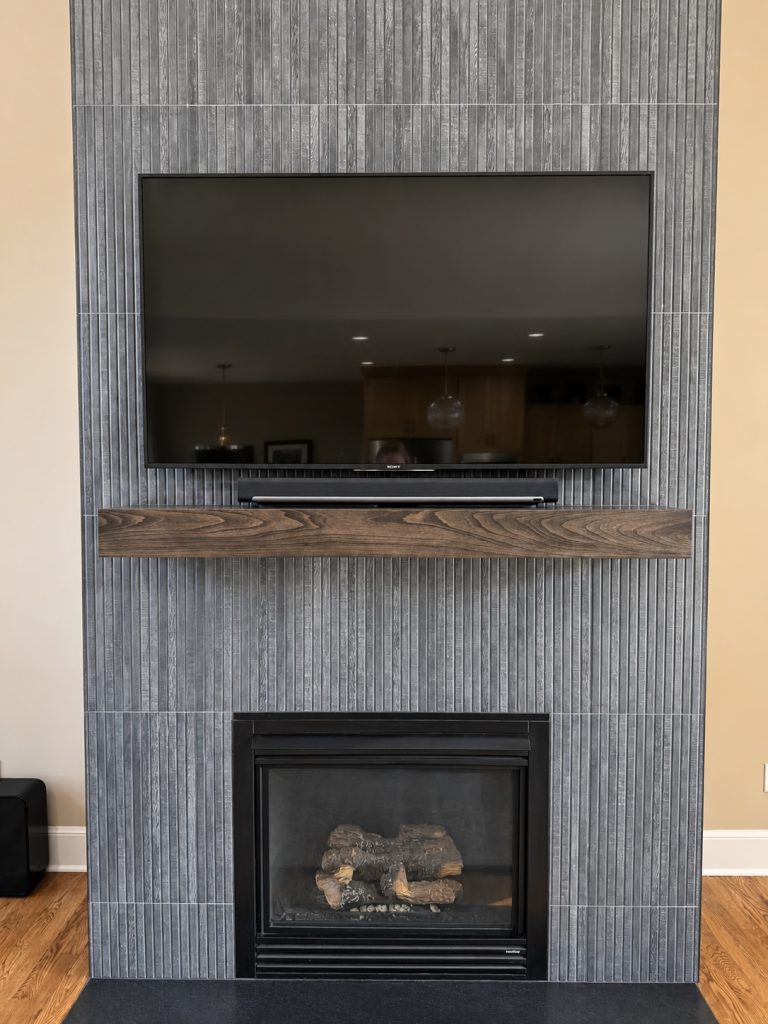 Remodeled fireplace with textured tile surround and wood mantel in a Kansas City living room