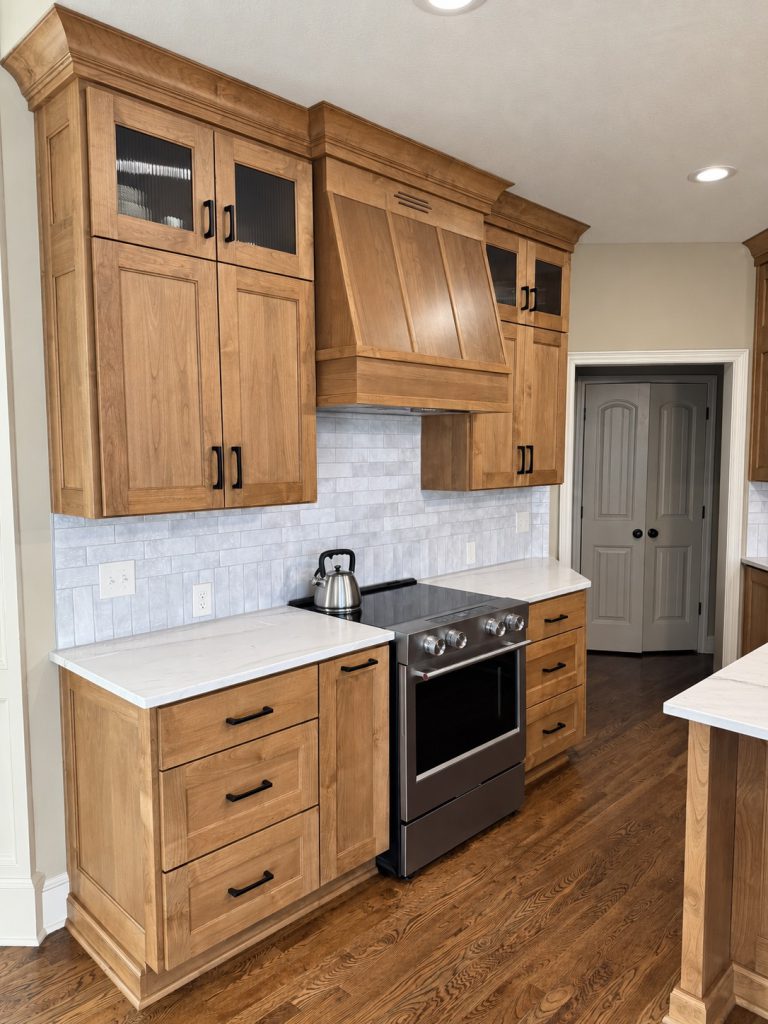Stainless range with a custom dark wood vent hood, subway tile backsplash, and white quartz counters in a remodeled Kansas City kitchen